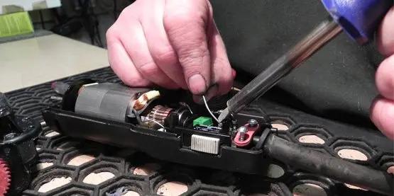 Person repairing electronic equipment with a screwdriver on a textured surface.