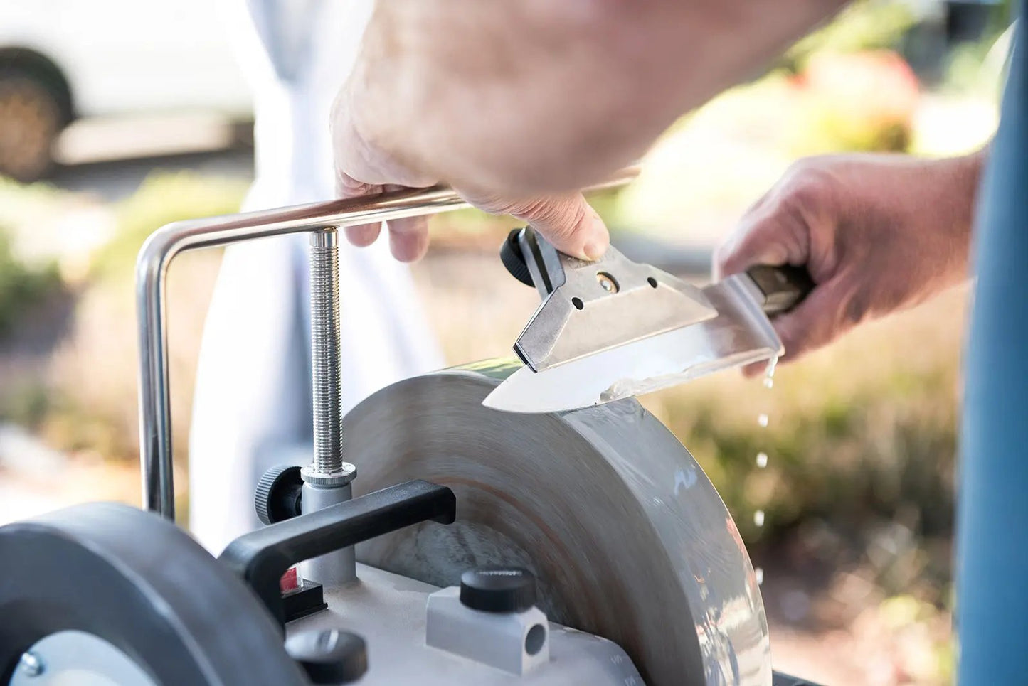 Person sharpening a blade on a stone wheel outdoors