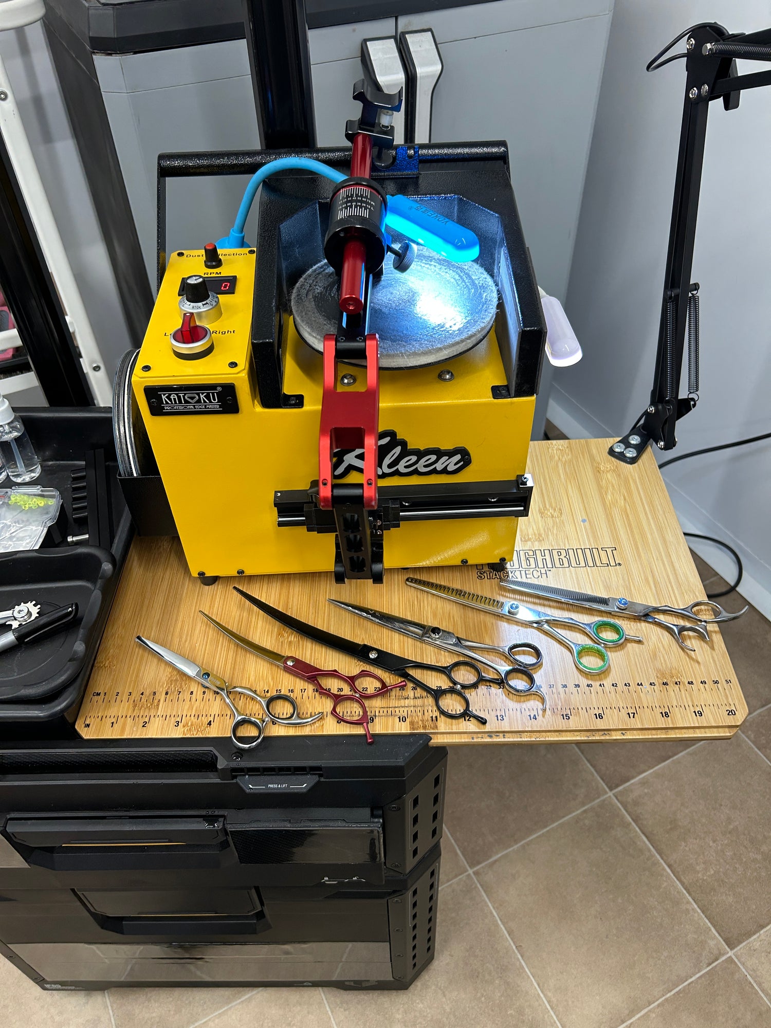Kleen sharpening machine with a red guide on a wooden to with 6 pairs f scissors. All mounted on a wheeled tool station