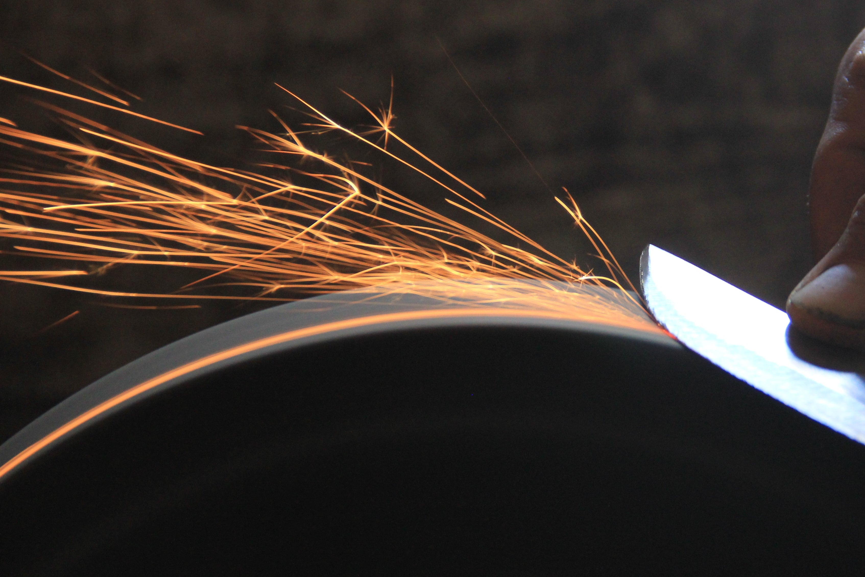 Person using a knife on a grinding wheel, with sparks flying.