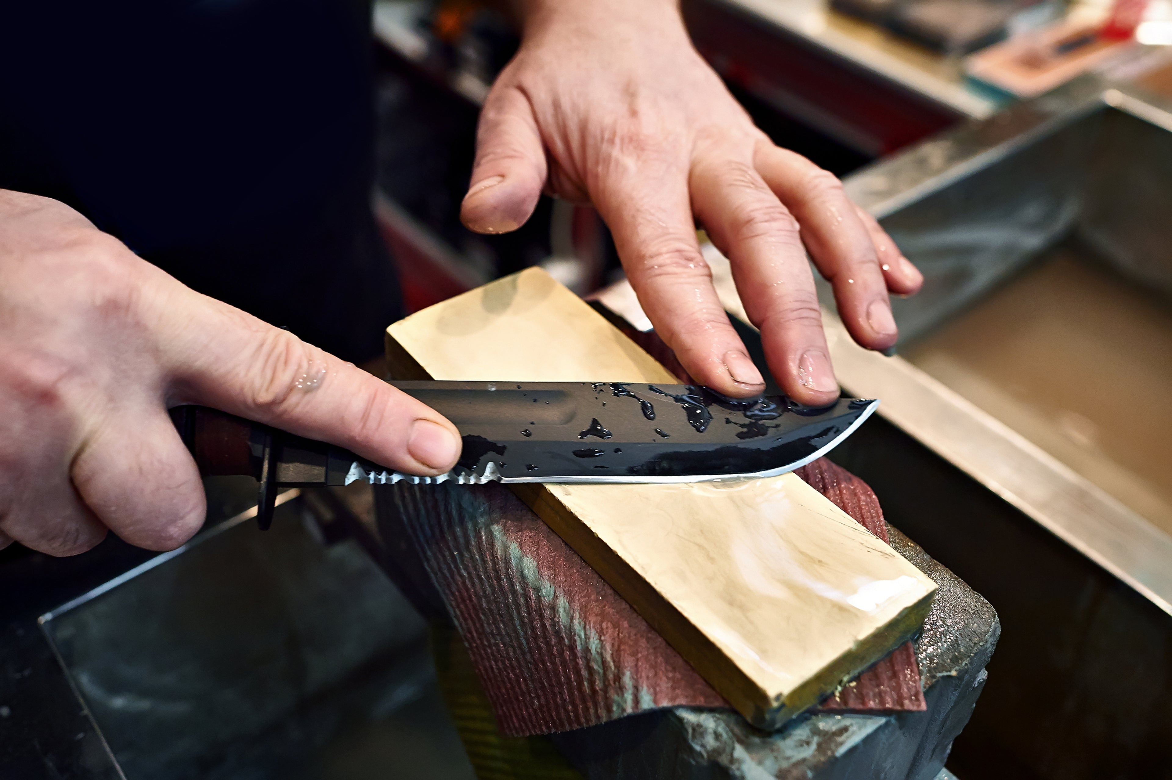 Person sharpening a knife on a stone with a blurred background
