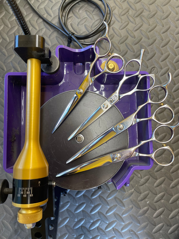 four Set of hairdressing shears with a shears holder on a  professional sharpening machine with textured gray plate 